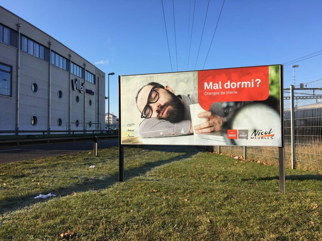 Photo d'une affiche de pub pour Nicol meubles devant leur concurrent villat meubles avec écrit: "bien dormi?".