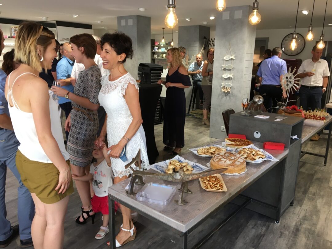 Houlmann Optique vu de l'intérieur où l'on voit plein de gens en train de parler ainsi que des apéritifs posés sur des tables.