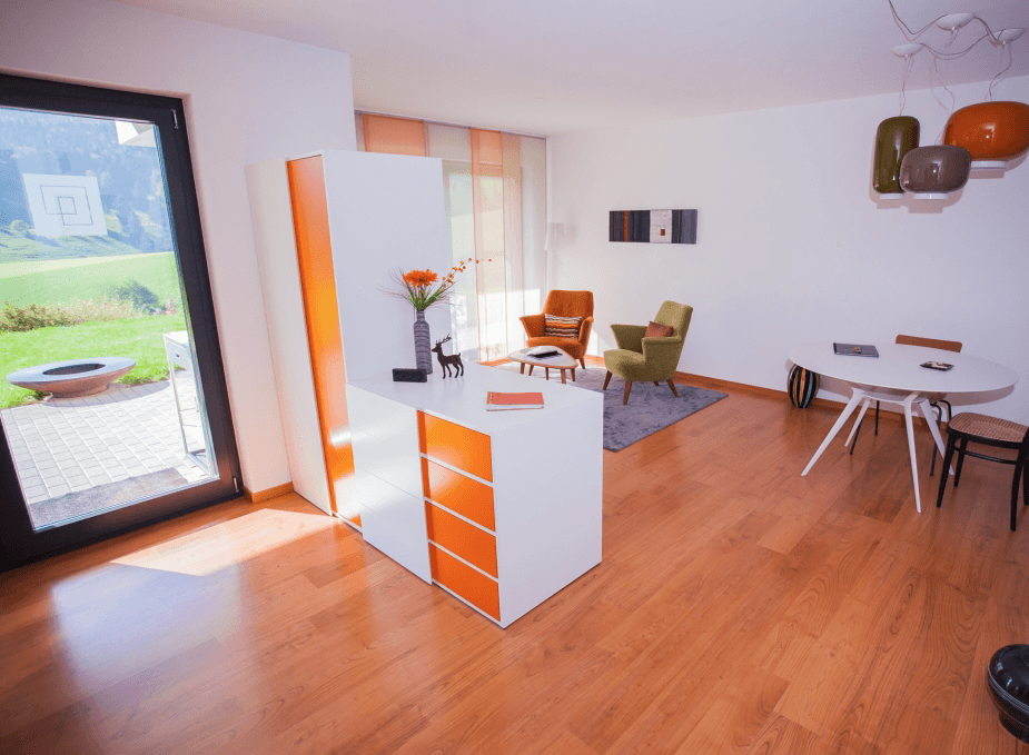 Salon avec parquet en bois brun, des fauteuils sur un tapis et des meubles.